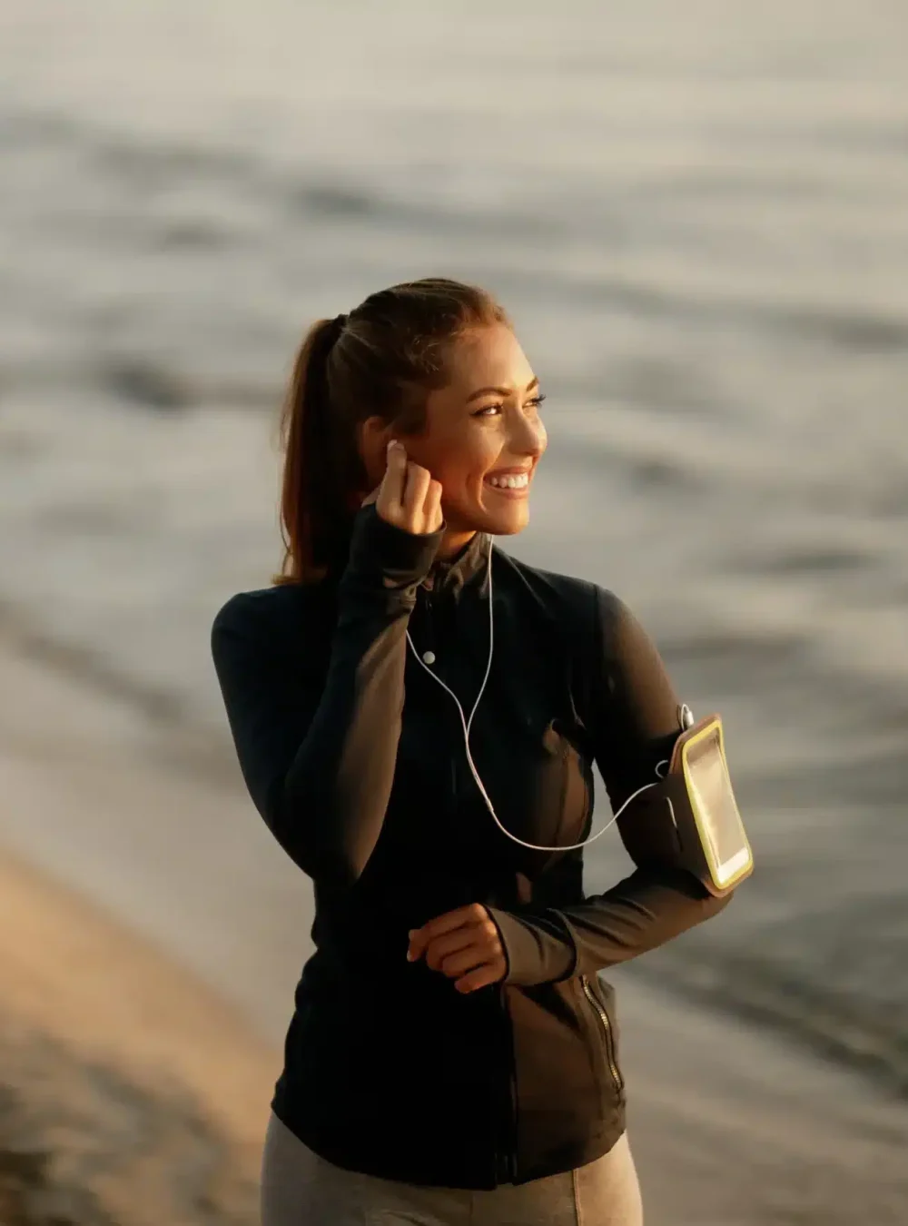 happy-sportswoman-getting-ready-morning-workout-listening-music-earphone-while-standing-beach-copy-space